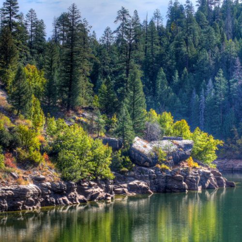 A serene lake surrounded by lush green trees and rocky shores, reflecting the vibrant colors of nature.