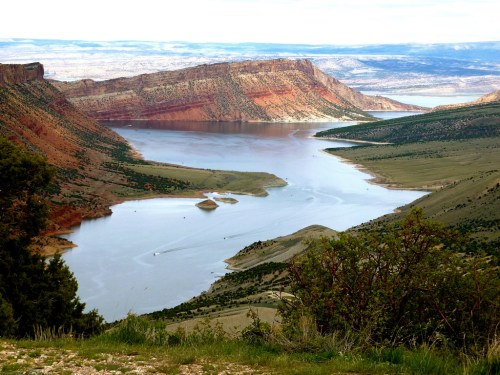 A scenic view of a winding river surrounded by red rock cliffs and green hills under a clear sky.