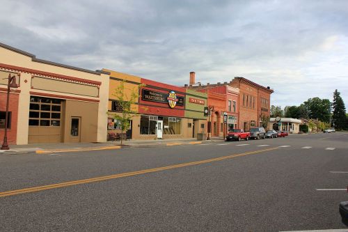 A quiet street scene featuring historic buildings, shops, and parked cars under a cloudy sky.
