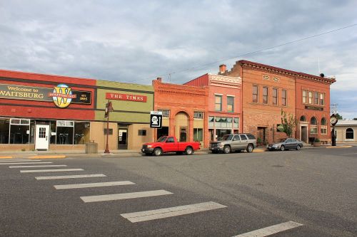 Historic buildings line a street in Waitsburg, featuring a welcome sign and a red pickup truck parked nearby.