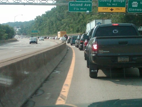 Traffic jam on a highway with vehicles lined up, approaching road signs for Second Ave and Liberty Bridge.