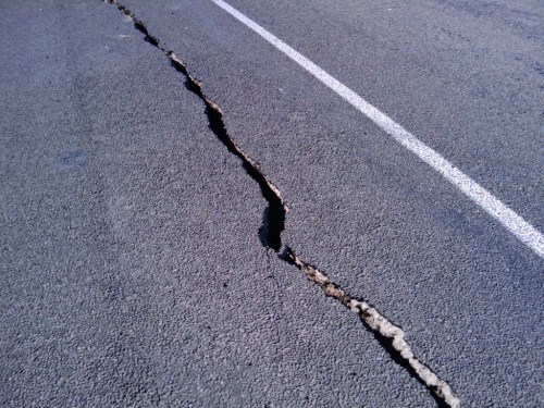 Cracked asphalt road with a deep fissure running through the surface, showing signs of damage.