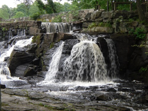 A serene waterfall cascading over rocky terrain, surrounded by lush greenery and natural stone formations.