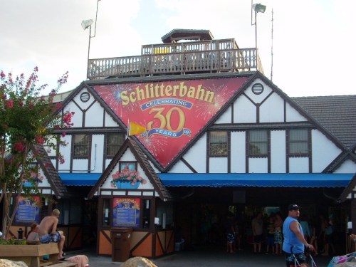 Exterior of Schlitterbahn water park, featuring a large banner celebrating 30 years, with people in swimwear nearby.