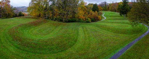 A scenic landscape featuring rolling green hills, winding paths, and colorful autumn trees in the background.