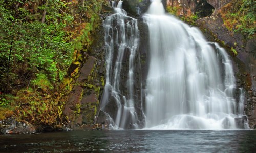 A serene waterfall cascading over rocky cliffs, surrounded by lush green foliage and reflecting in the calm water below.