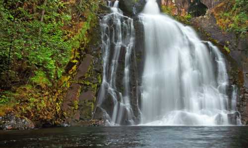 A serene waterfall cascading over rocky cliffs, surrounded by lush green foliage and reflecting in the calm water below.