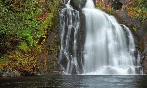 A serene waterfall cascading over rocky cliffs, surrounded by lush green foliage and reflecting in the calm water below.