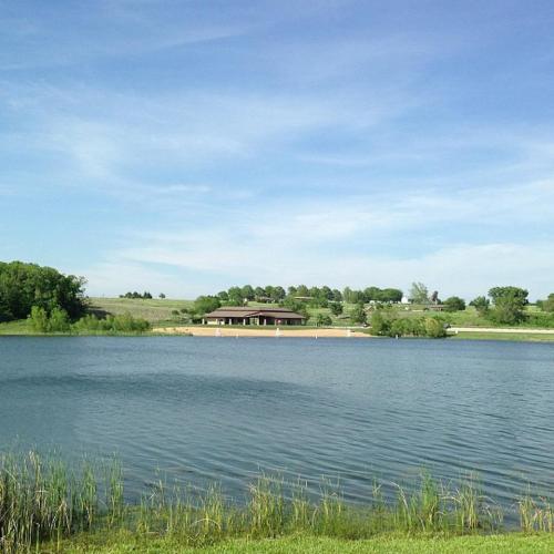 A serene lake scene with a small building in the distance, surrounded by greenery and a clear blue sky.