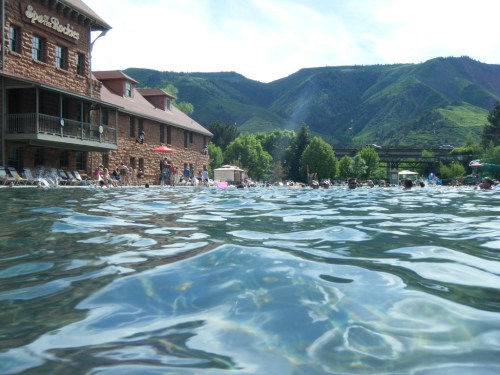 A serene pool scene with mountains in the background, surrounded by lounge chairs and trees under a clear sky.
