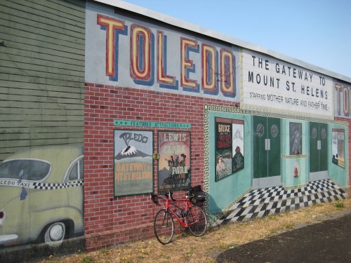 Mural on a building featuring "Toledo" and "Gateway to Mount St. Helens," with a bicycle parked in front.