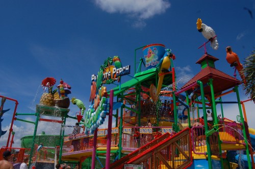 Colorful water park structure with slides, water features, and playful decorations under a bright blue sky.