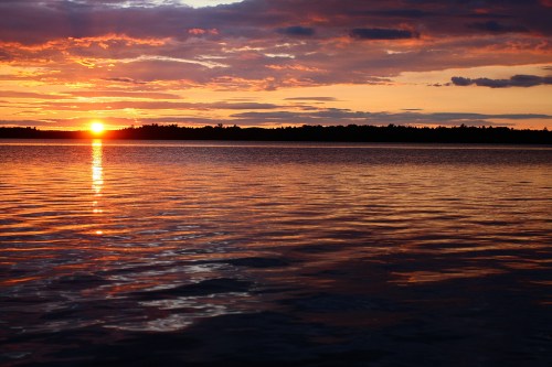 A serene sunset over a calm lake, with vibrant orange and purple hues reflecting on the water's surface.