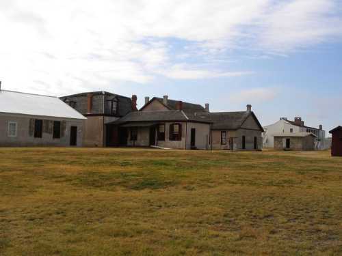 Historic buildings on a grassy field under a cloudy sky, showcasing a mix of architectural styles.