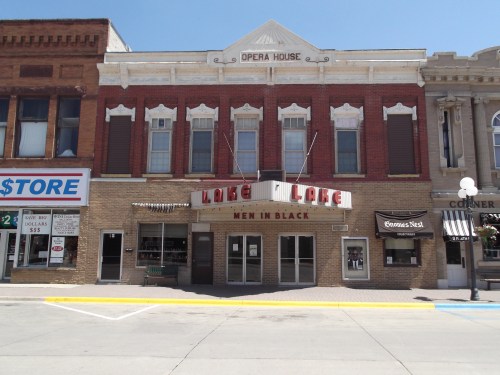 Historic building with "Opera House" sign, featuring a marquee for "Men in Black" and nearby shops on a sunny day.