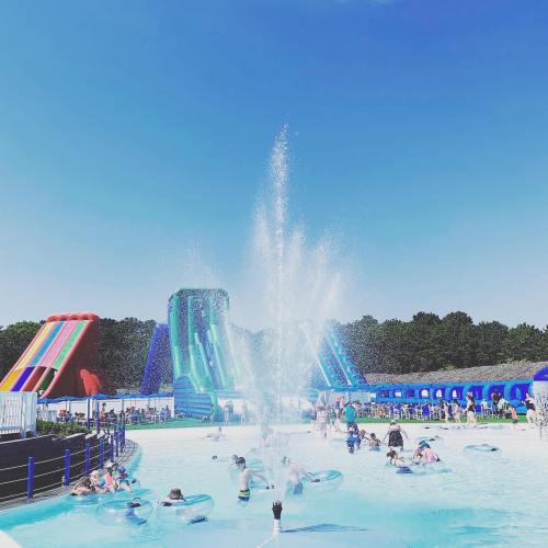 A vibrant water park scene with colorful slides, a large pool, and people enjoying the sun and water activities.