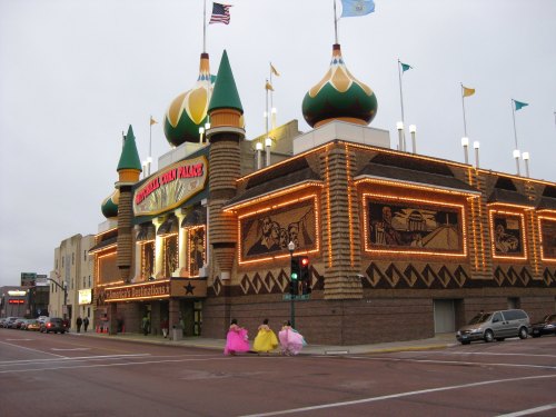 Colorful building with a castle-like design, featuring bright lights and flags, and three people in pink dresses walking by.