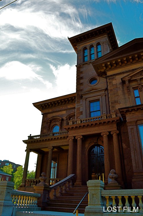 Historic building with ornate architecture, featuring columns and a tower, set against a blue sky with wispy clouds.