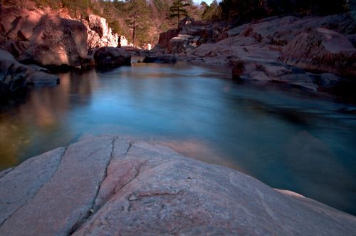 A serene river flows between rocky banks, surrounded by trees and a tranquil landscape under soft lighting.