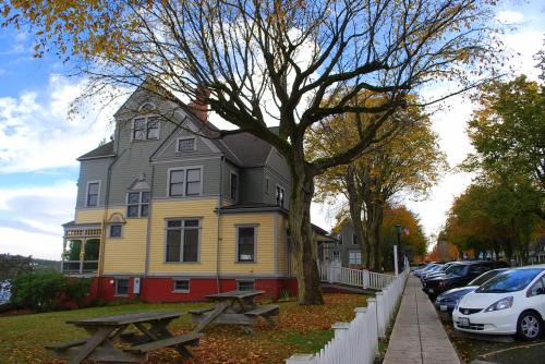 A colorful Victorian house beside a tree-lined street with parked cars and picnic tables in autumn.