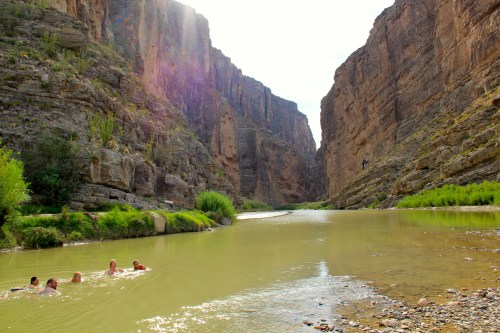 A group of people swimming in a river surrounded by tall, rocky canyon walls and lush greenery.