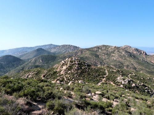 A scenic view of rolling green hills and rocky terrain under a clear blue sky.