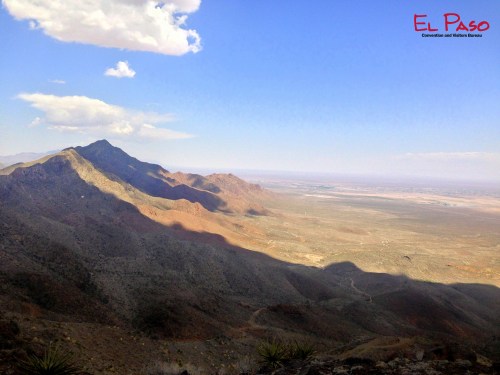 A panoramic view of rugged mountains and valleys under a blue sky with scattered clouds, showcasing the El Paso landscape.