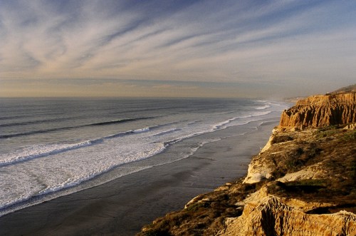 A scenic view of a coastline with cliffs, gentle waves, and a cloudy sky at sunset.