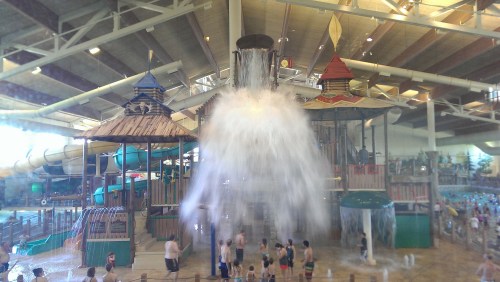 A water park scene featuring a large water feature, colorful structures, and people enjoying the splash area.