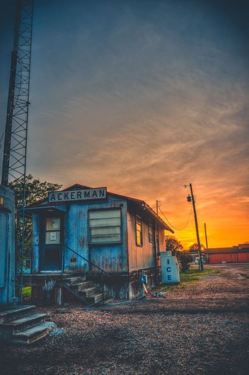 A weathered blue building labeled "Ackerman" at sunset, with a nearby ice vending machine and power lines.