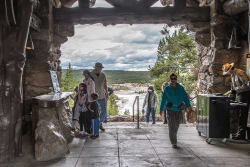 A stone entrance with visitors, including children, looking at displays and a scenic view of nature outside.