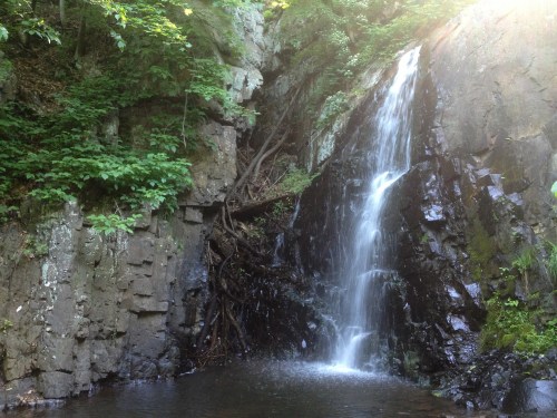 A serene waterfall cascading down rocky cliffs, surrounded by lush greenery and trees.