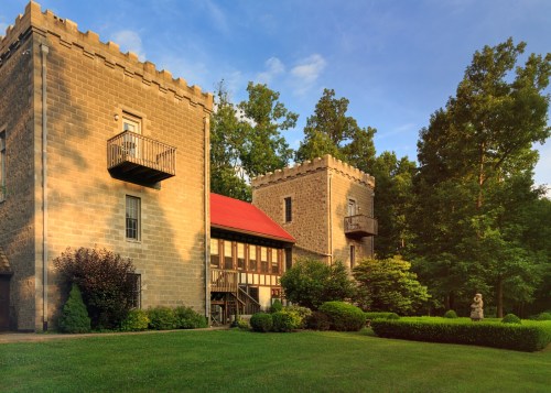 Two stone towers with balconies, surrounded by lush greenery and a manicured lawn under a clear blue sky.