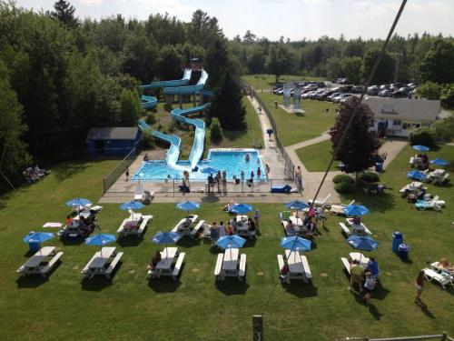 Aerial view of a pool area with water slides, picnic tables, and people enjoying a sunny day outdoors.