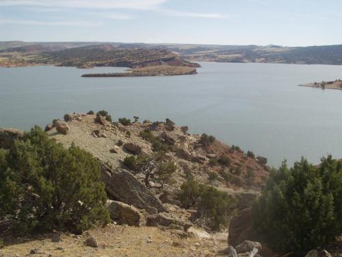 A serene lake surrounded by rocky terrain and distant hills under a clear blue sky.