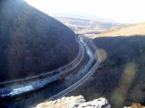 A winding river and roads nestled between two mountains under a clear sky.