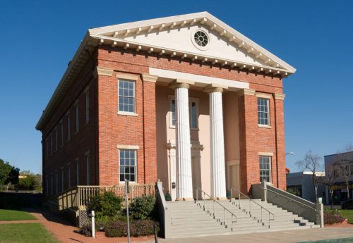 Historic brick building with white columns and a pediment, set against a clear blue sky.