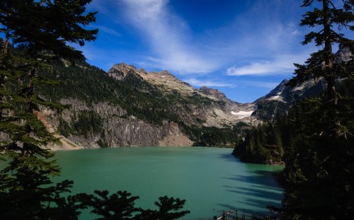 A serene lake surrounded by mountains and trees under a clear blue sky.