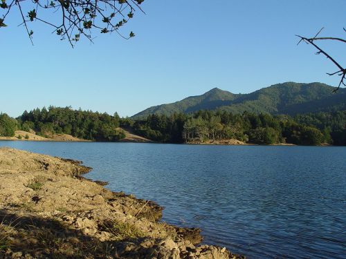 A serene lake surrounded by green hills and trees under a clear blue sky.