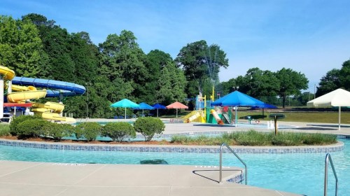 A sunny water park scene featuring colorful slides, play structures, and shaded areas with umbrellas.