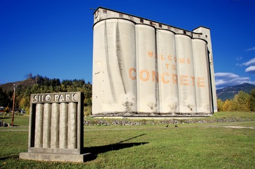 A large concrete silo with "Welcome to Concrete" painted on it, next to a sign for Silo Park in a grassy area.