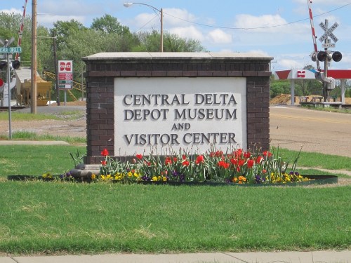 Sign for the Central Delta Depot Museum and Visitor Center, surrounded by colorful flowers and green grass.