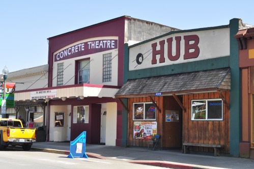 Two storefronts in a small town: a theater labeled "Concrete Theatre" and a building labeled "HUB," with a sunny sky.