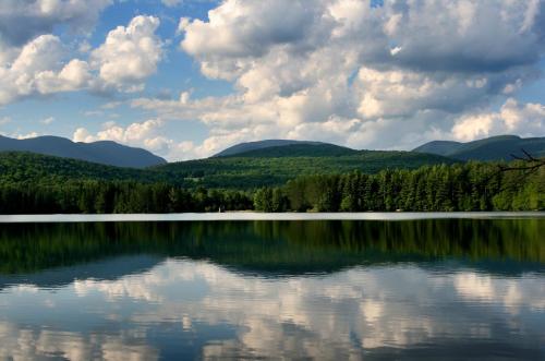 A serene lake surrounded by lush green mountains and a blue sky filled with fluffy clouds, reflecting on the water's surface.