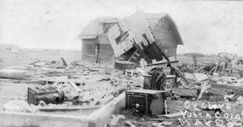 A damaged house surrounded by debris, showcasing the aftermath of a natural disaster. Black and white photo.