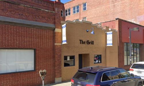 Exterior view of a restaurant called "The Grill," featuring brick walls and a sign, with a parked vehicle in front.