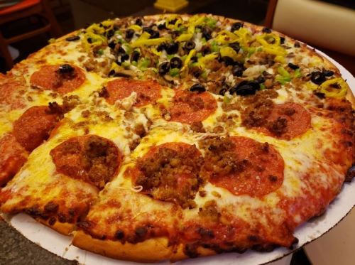 A large pizza divided into two halves: one with pepperoni and sausage, the other topped with olives, peppers, and onions.