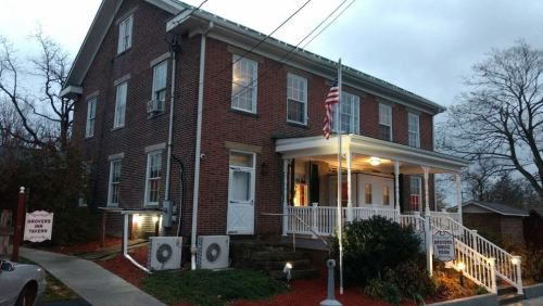 Historic brick building with a porch, American flag, and sign for "Drove's Inn Tavern," surrounded by trees and evening light.