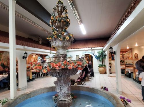 A decorative fountain with flowers in a cozy restaurant interior, featuring dining areas and warm lighting.