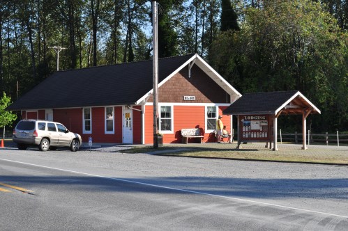 A red and brown building with a sign for lodging, surrounded by trees and a gravel road.